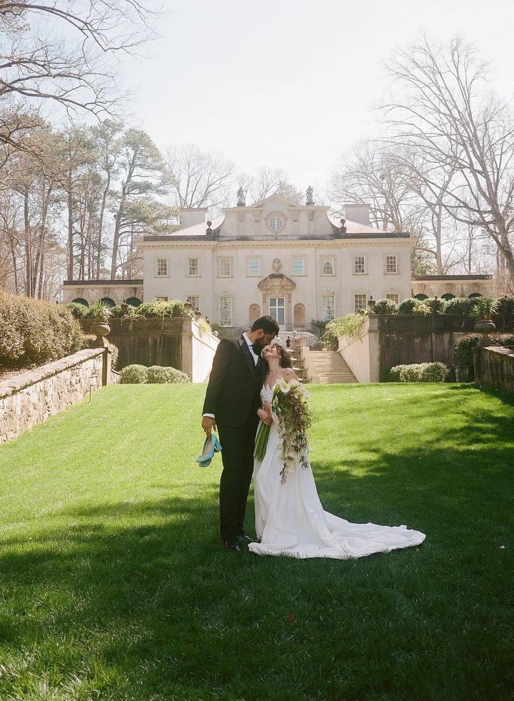 Bride and groom standing together in a formal pose with the historic Swan House mansion in the background, showcasing its classic architecture and manicured gardens.